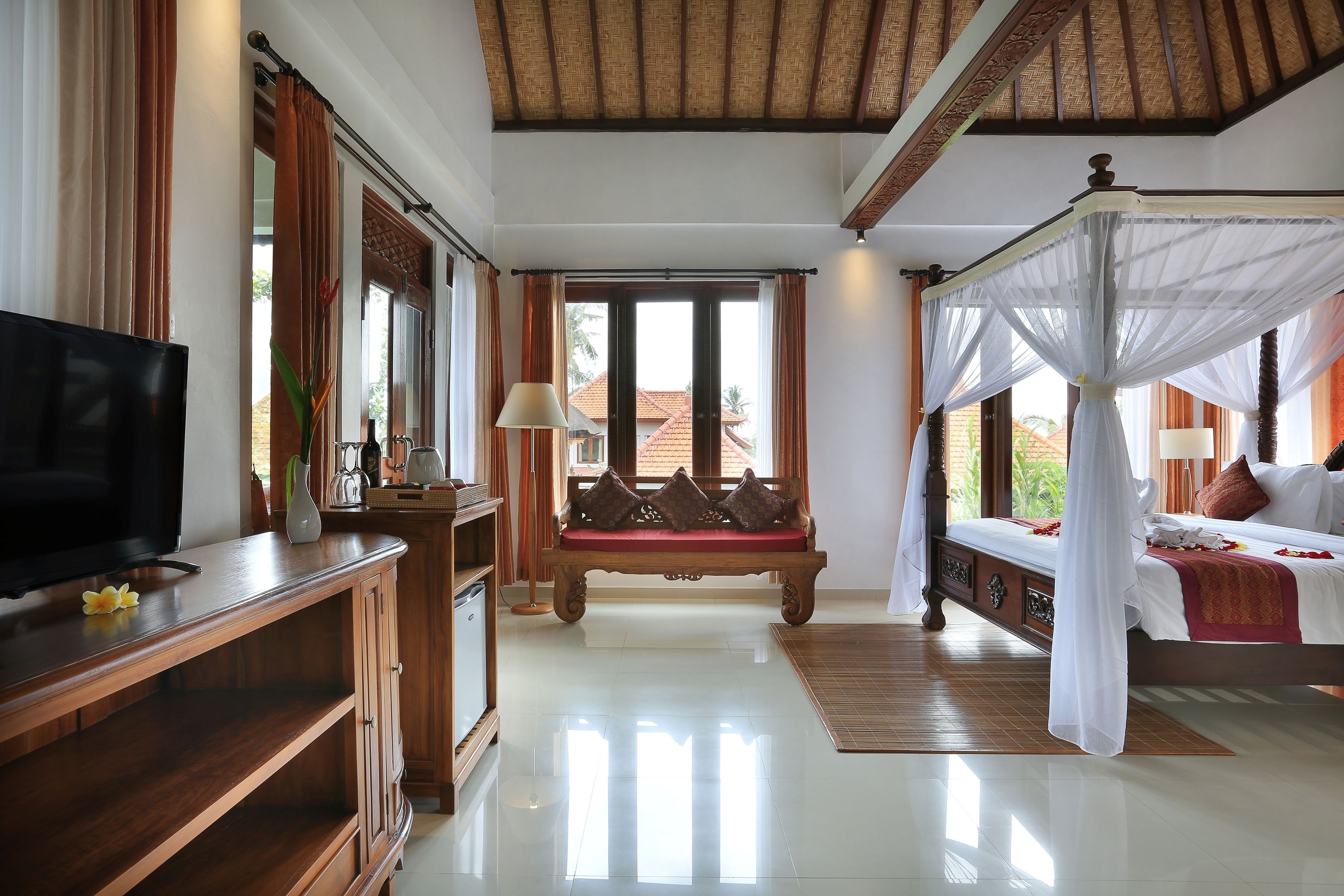 A bedroom with a bed, a TV, a bench, and a window with curtains.