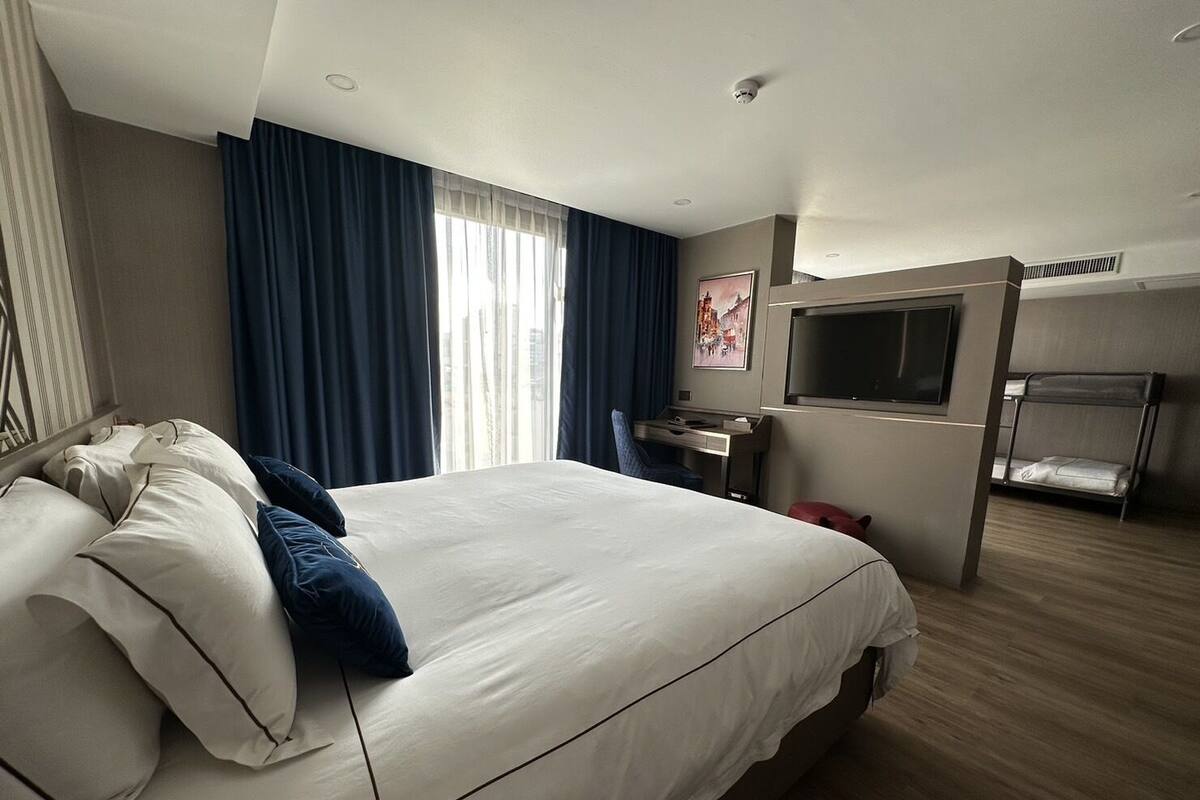A hotel room with a large bed, a desk, a TV, and a bunk bed.