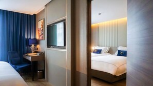 A hotel room with a bed, a desk with a lamp, a television, and a large window with curtains. - GLOW Sukhumvit 5 by Centropolis (Bangkok)