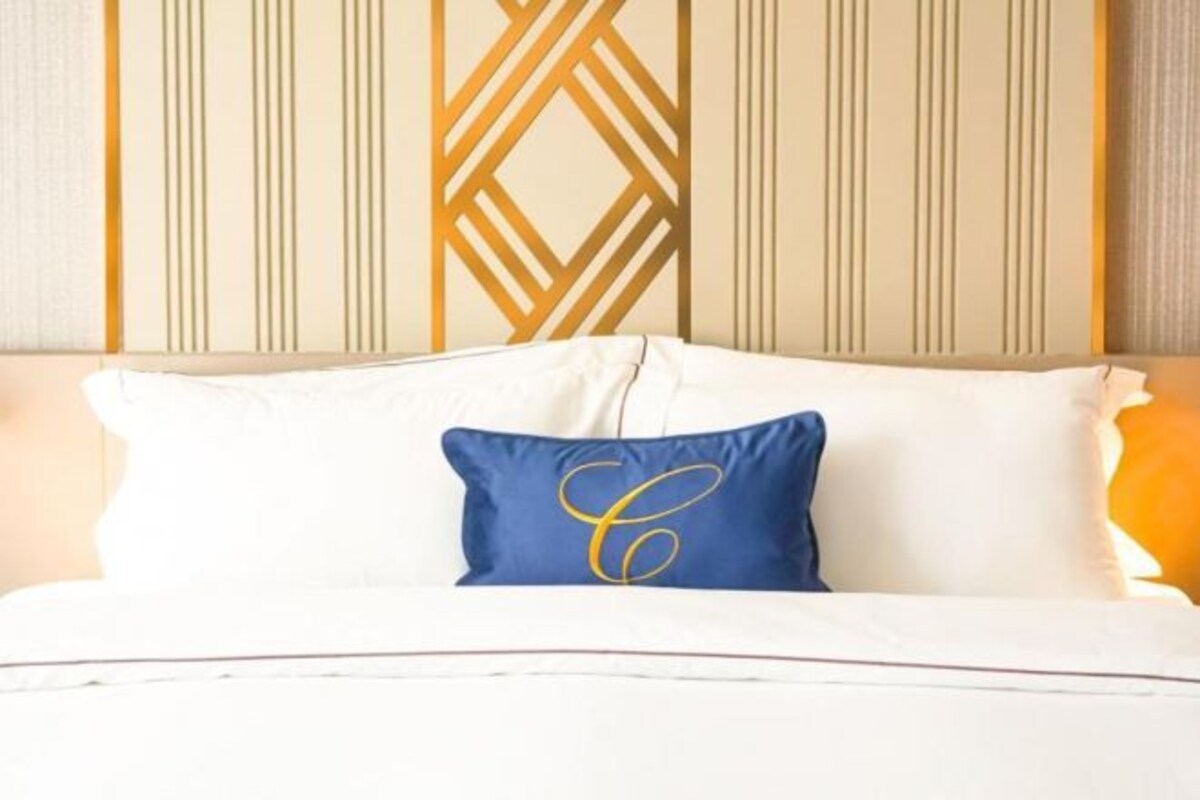 A bed with white bedding and a blue pillow with a gold monogram.