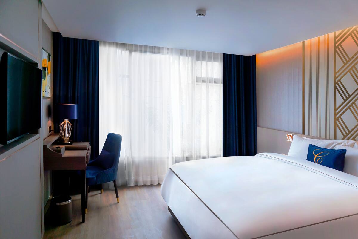 A hotel room with a bed, a desk, a chair, a TV, and a window with curtains.