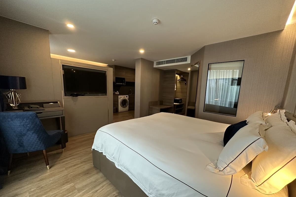 A hotel room with a bed, a desk, a chair, a washing machine, and a mirror.