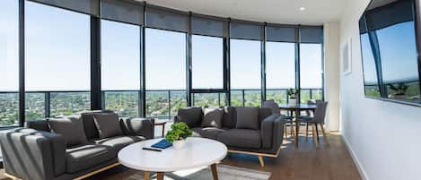 A modern living room with a large window, a sofa, a coffee table, and a dining area.