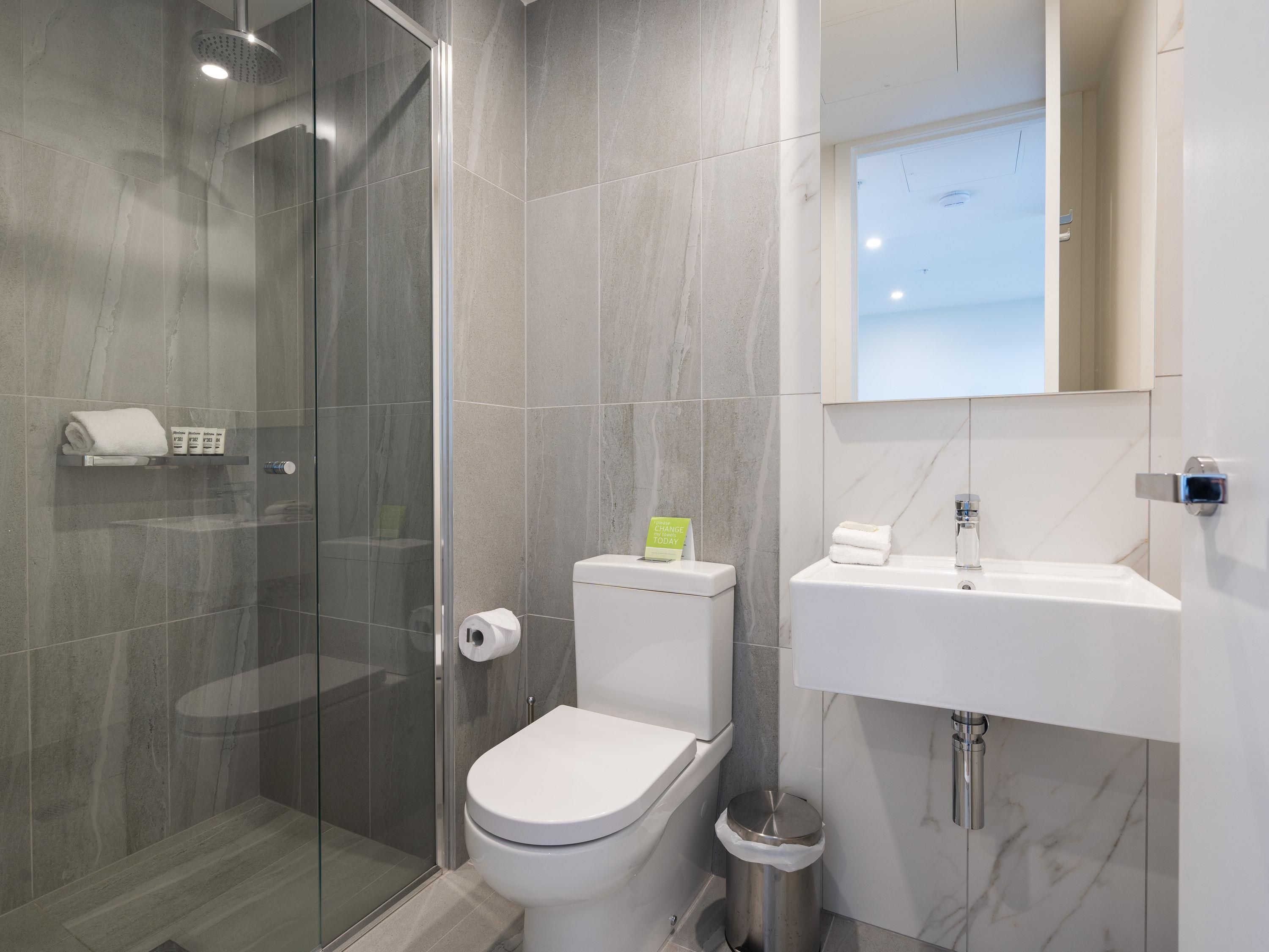 Un baño moderno con cabina de ducha de vidrio, inodoro y lavamanos con espejo.