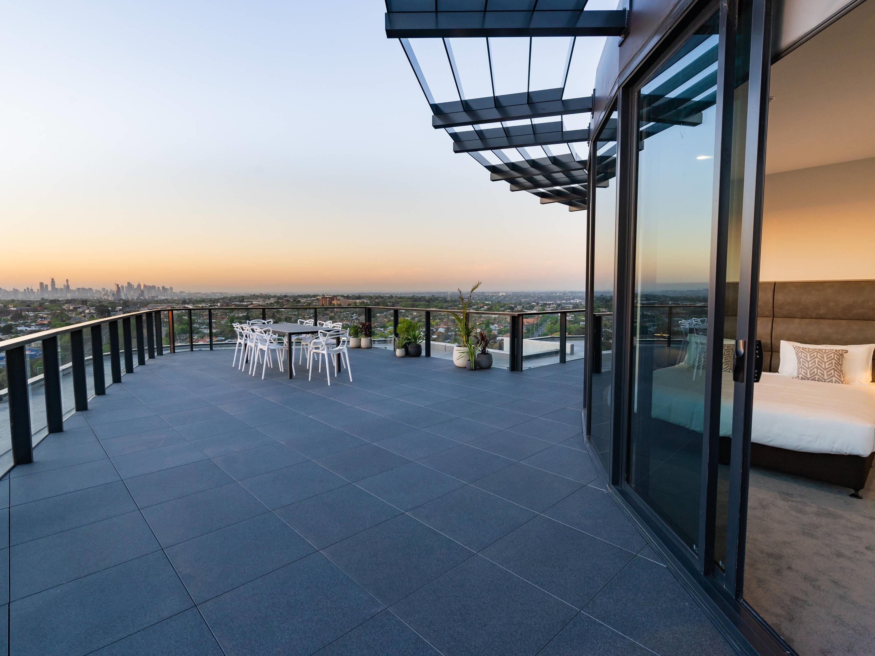 Ein moderner Balkon mit Glastür zum Schlafzimmer, einem Esstisch mit Stühlen und Blick auf die Stadt.