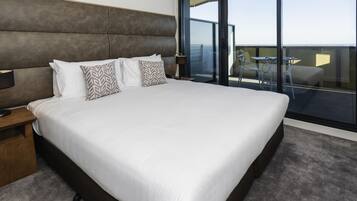 Una habitación de hotel moderna con una cama grande, una mesita de noche, un escritorio y un balcón con mesa y sillas.