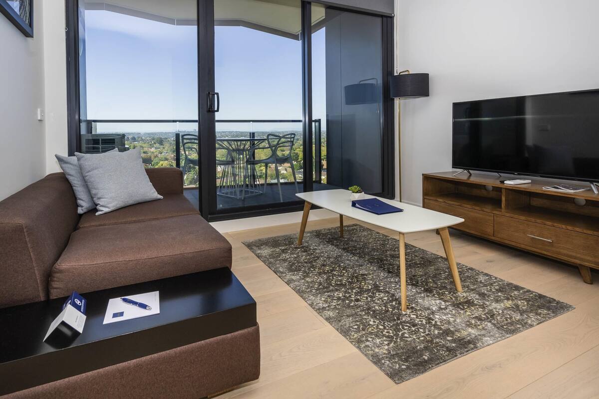 A modern living room with a brown sofa, a white coffee table, and a TV on a wooden stand.