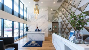 Una zona de recepción moderna con un mostrador de mármol, una recepcionista y un amplio ventanal con vistas al estacionamiento.