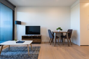 A modern living room with a flat-screen TV, a small table with a plant, and two chairs. - The Sebel Melbourne Malvern (Malvern East)