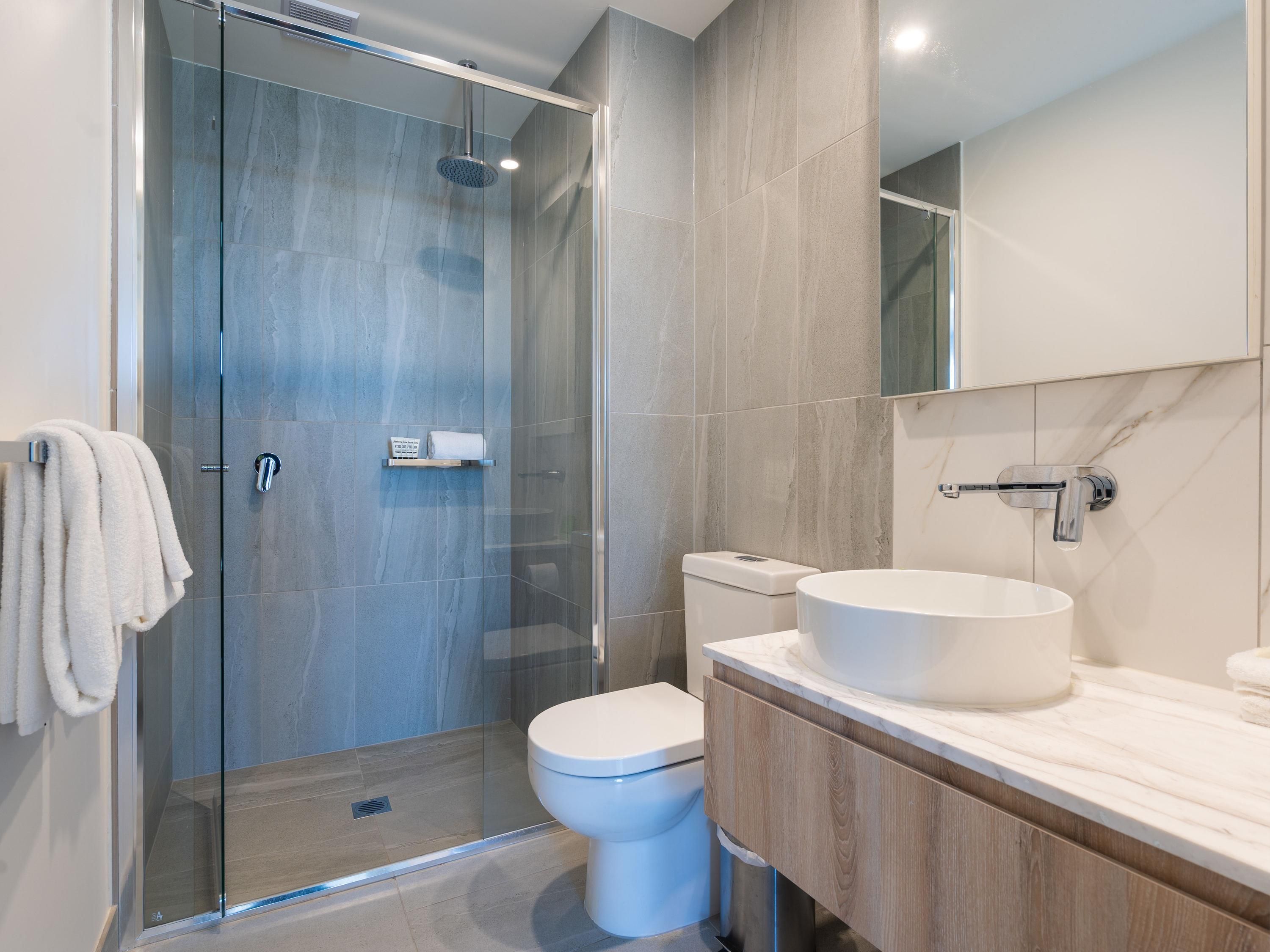 A modern bathroom with a glass-enclosed shower, a white toilet, and a large sink with a marble countertop.