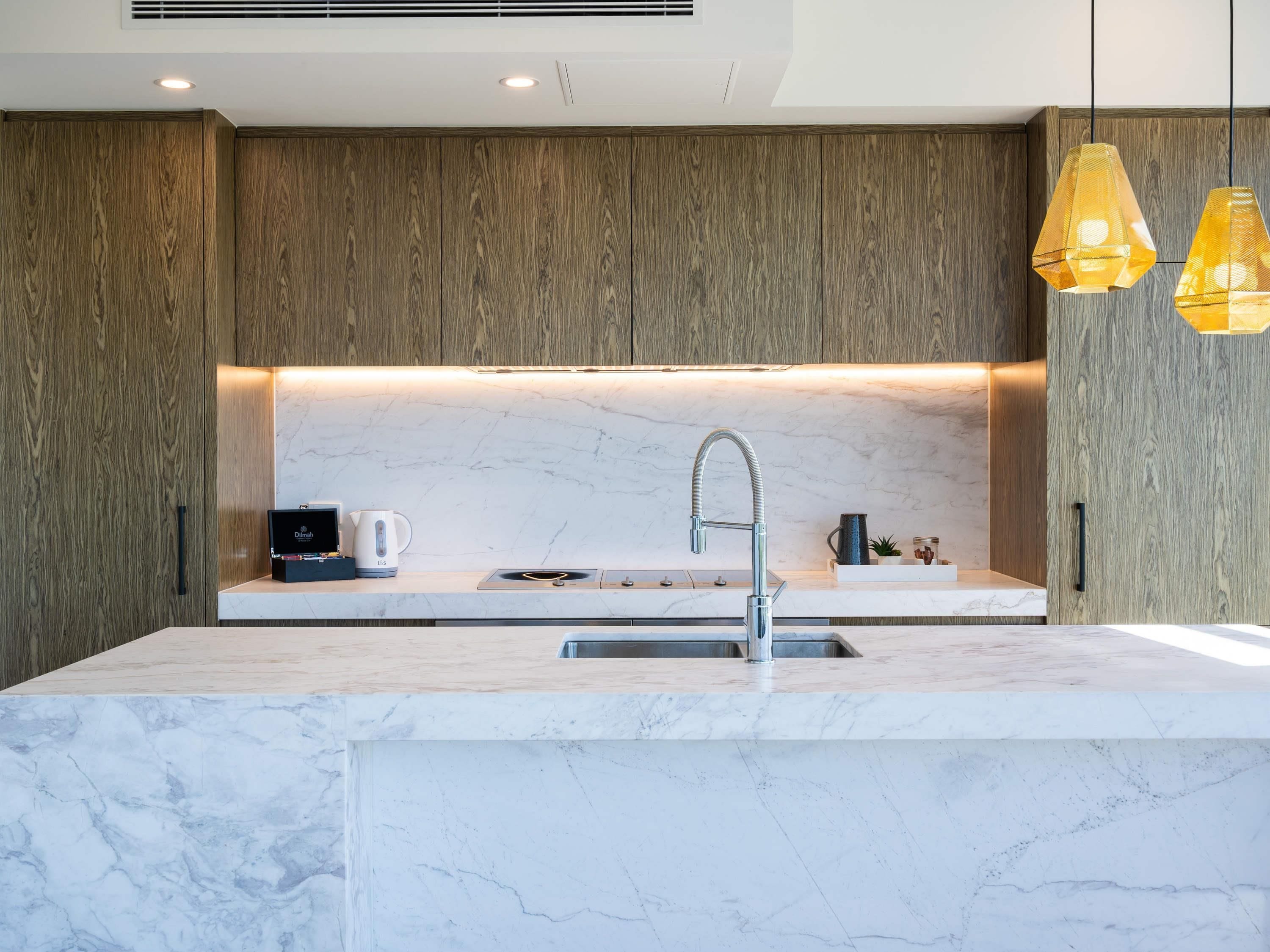 A modern kitchen with a marble countertop, stainless steel sink, and wooden cabinetry.