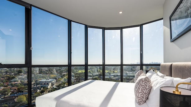 Un dormitorio moderno con una cama grande, vistas a un paisaje urbano y un diseño de ventana curva.