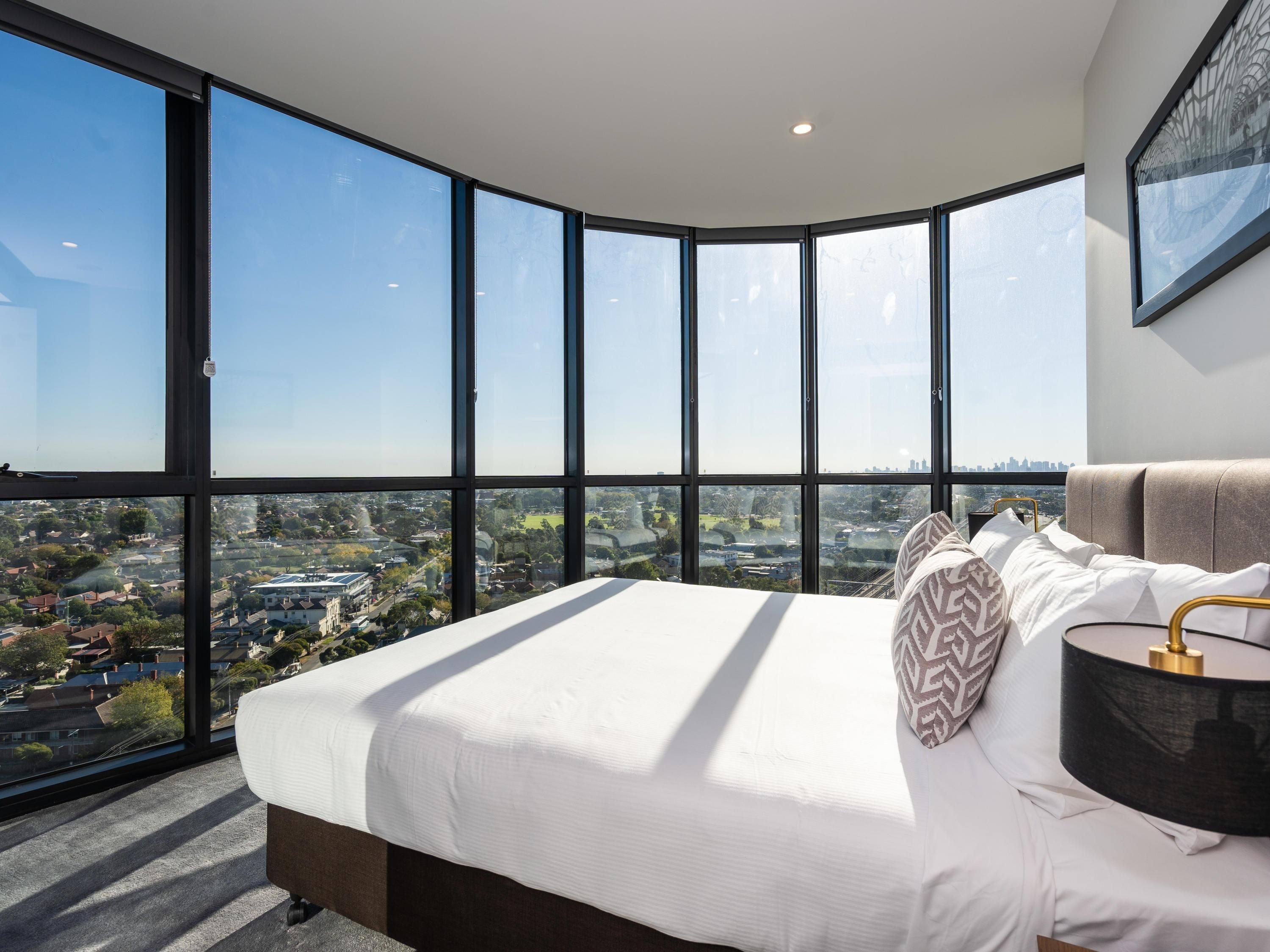 A bedroom with a large bed, a view of a cityscape through floor-to-ceiling windows, and a modern design.