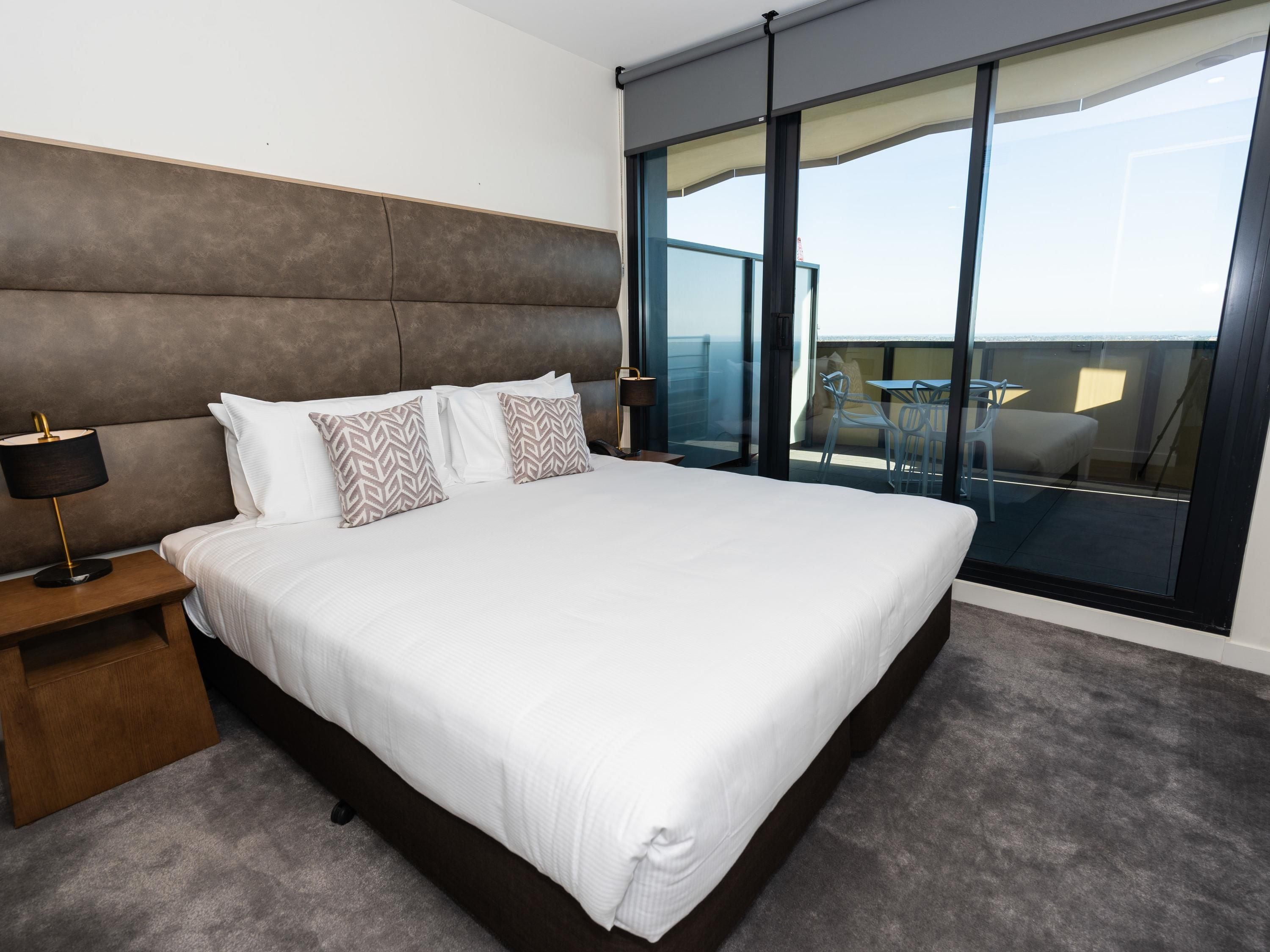 Een moderne hotelkamer met een groot bed, een nachtkastje, een lamp en uitzicht op het buitenbalkon.