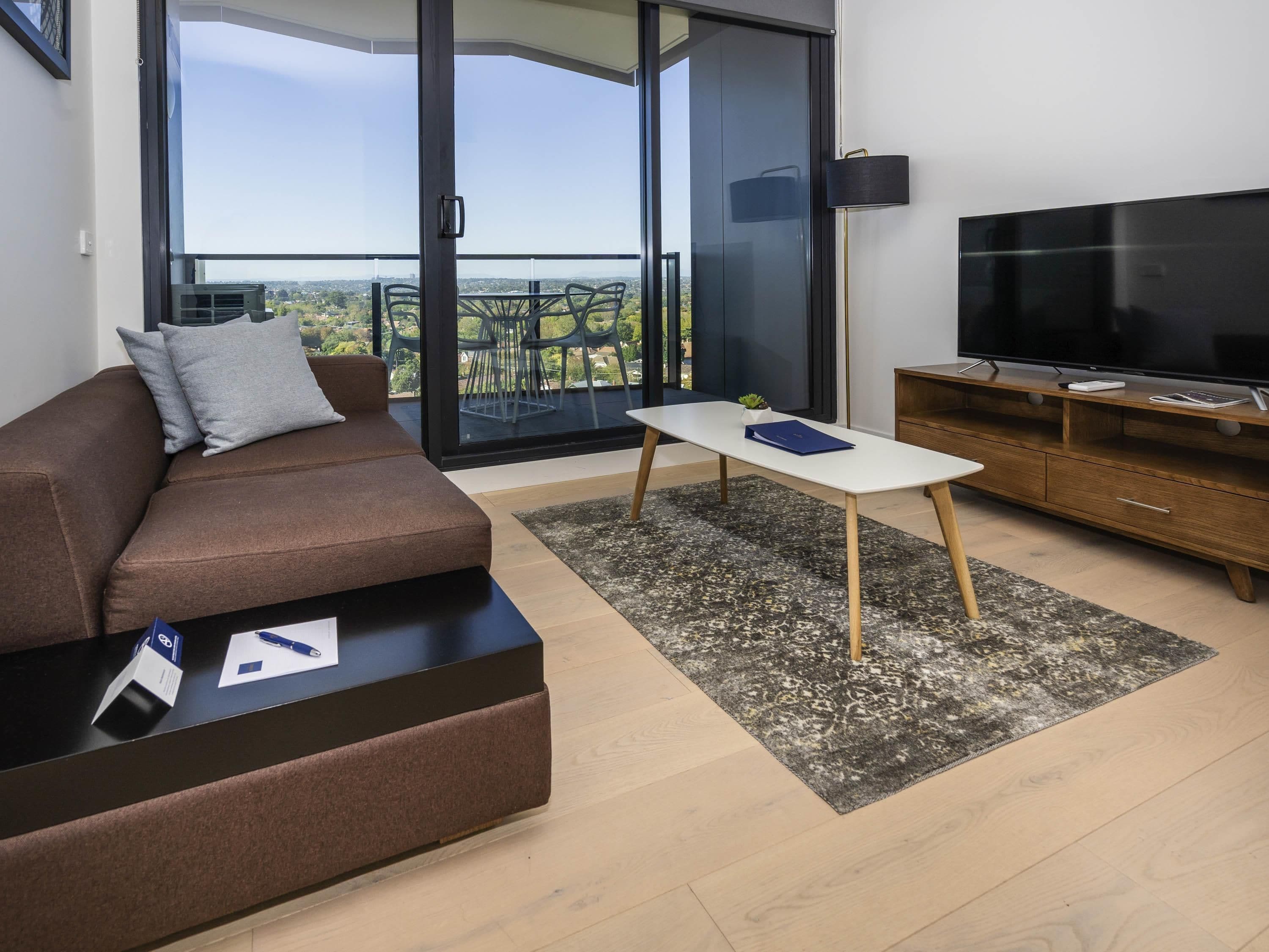 A modern living room with a sofa, a coffee table, a TV, and a balcony with a city view.