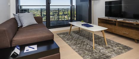 Ein modernes Wohnzimmer mit einer Couch, einem Couchtisch, einem Fernseher und einem Balkon mit Blick auf die Stadt.