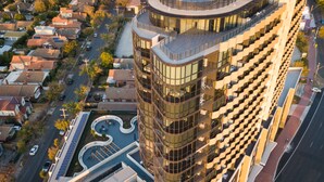 Un moderno edificio de gran altura con fachada de vidrio curva, jardín en la azotea y zona de estacionamiento.