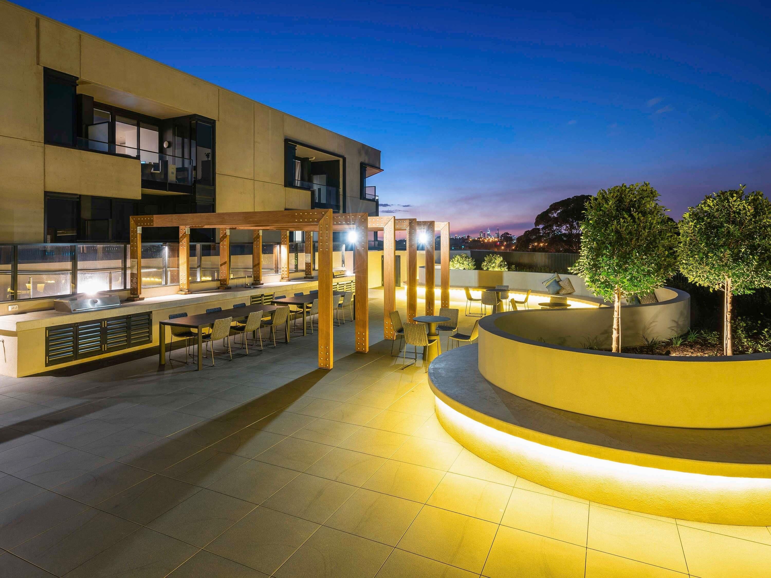 Un área de comedor al aire libre con piscina, asientos y vista del horizonte de la ciudad al atardecer.