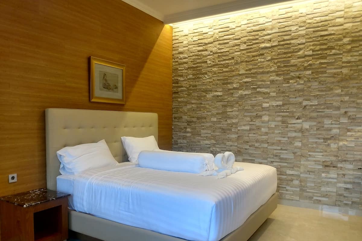 Una cama bien hecha con sábanas blancas y un cabecero, una mesita de noche de madera y una pared con textura de piedra.