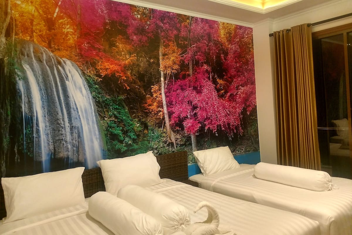 Habitación de hotel con dos camas, un mural de una cascada y follaje otoñal, y vista al exterior a través de una ventana con cortinas.