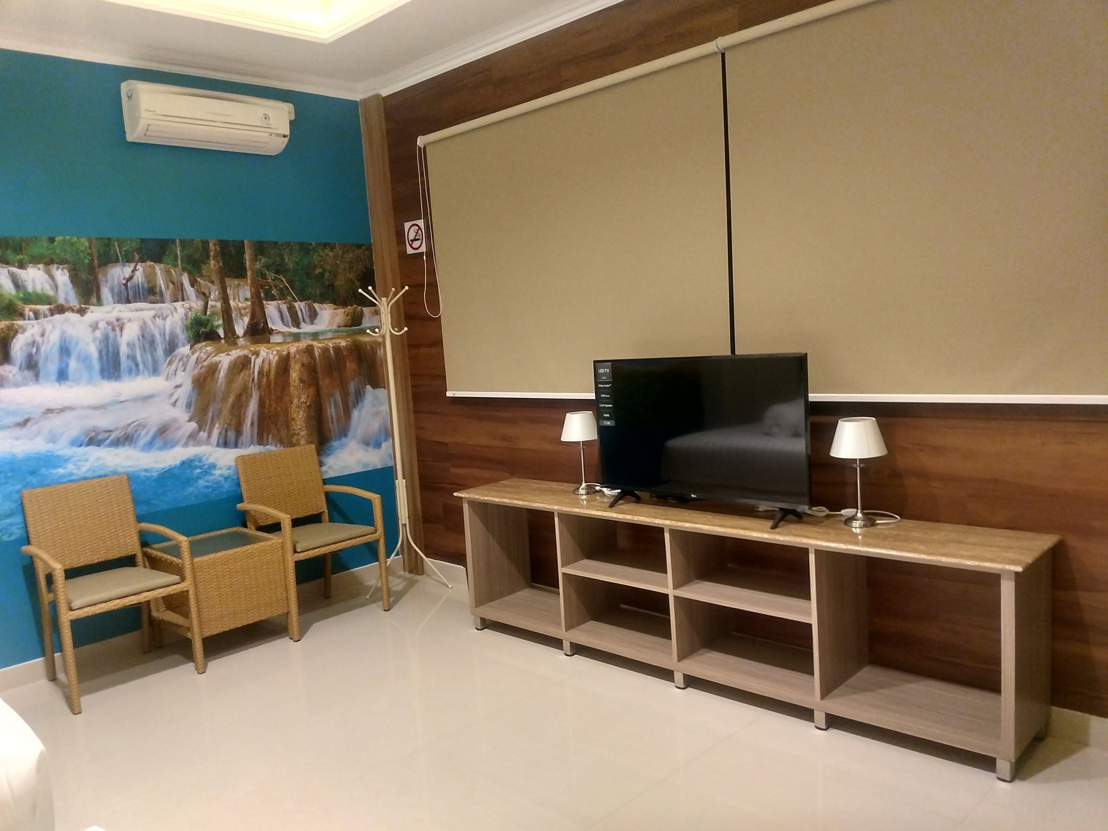 Quarto com televisão sobre suporte de madeira, duas cadeiras, tela fixada na parede e um mural de uma cachoeira.