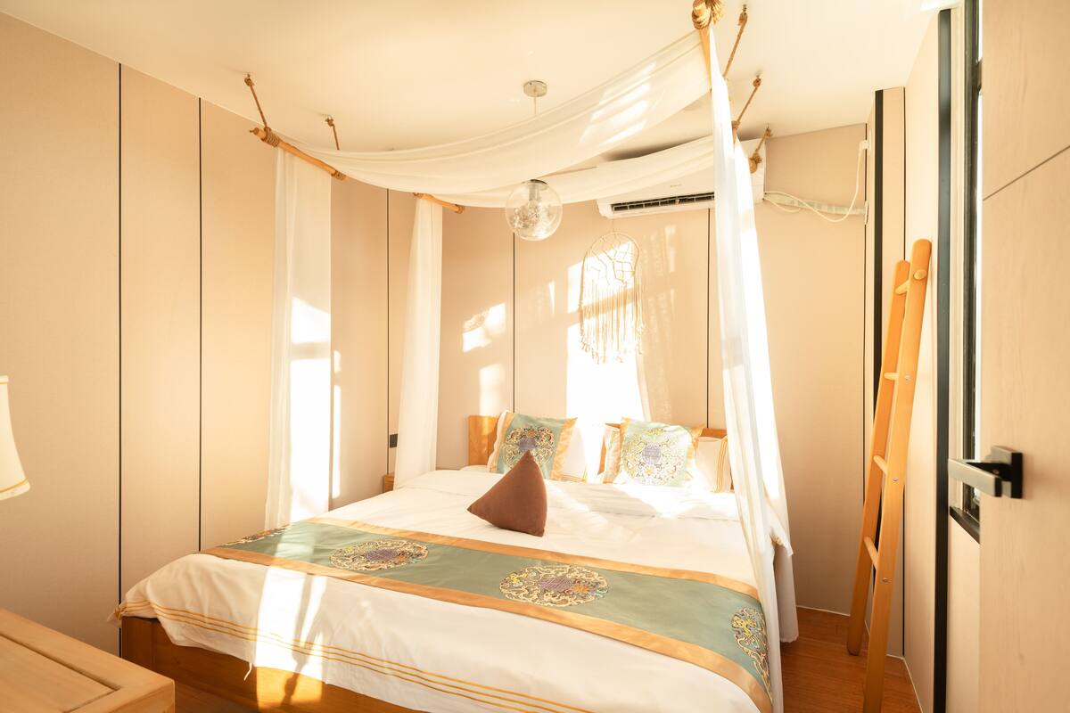 A bedroom with a canopy bed, a bedside table, and a window with curtains.