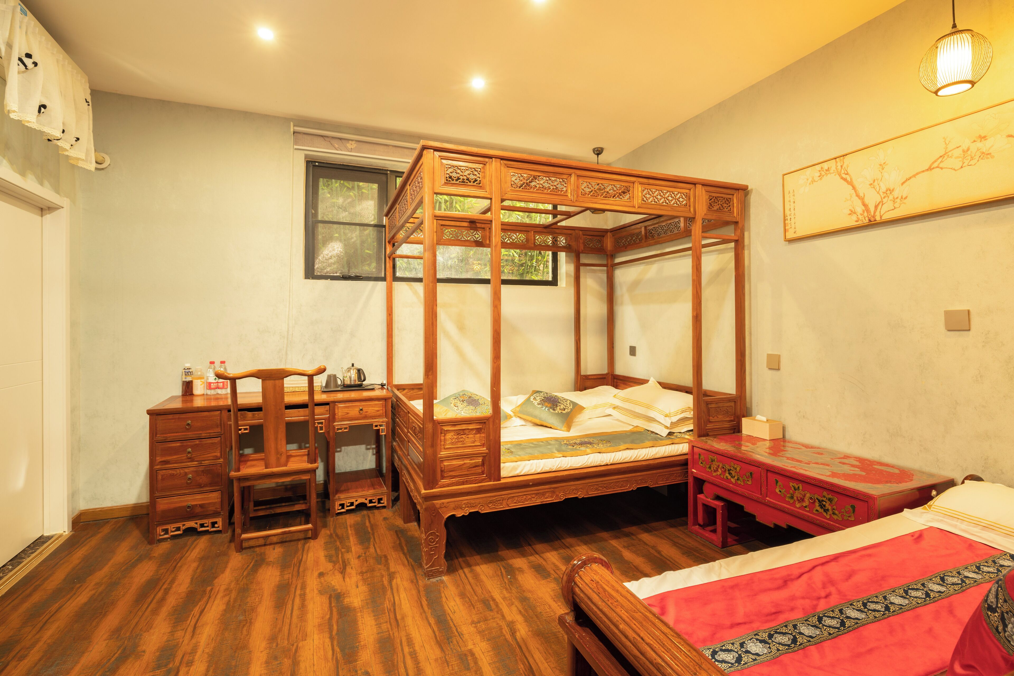 A traditional four-poster bed with a wooden desk and chair, a red dresser, and a painting on the wall.