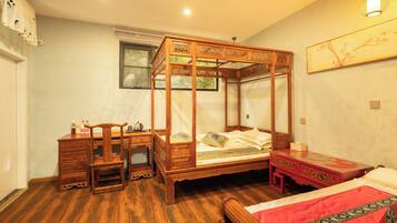 A traditional four-poster bed with a wooden desk and chair, a red dresser, and a painting on the wall.