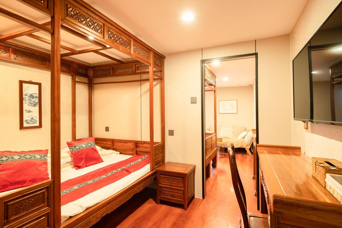 A traditional Japanese-style room with a four-poster bed, a wooden desk, and a television on the wall.