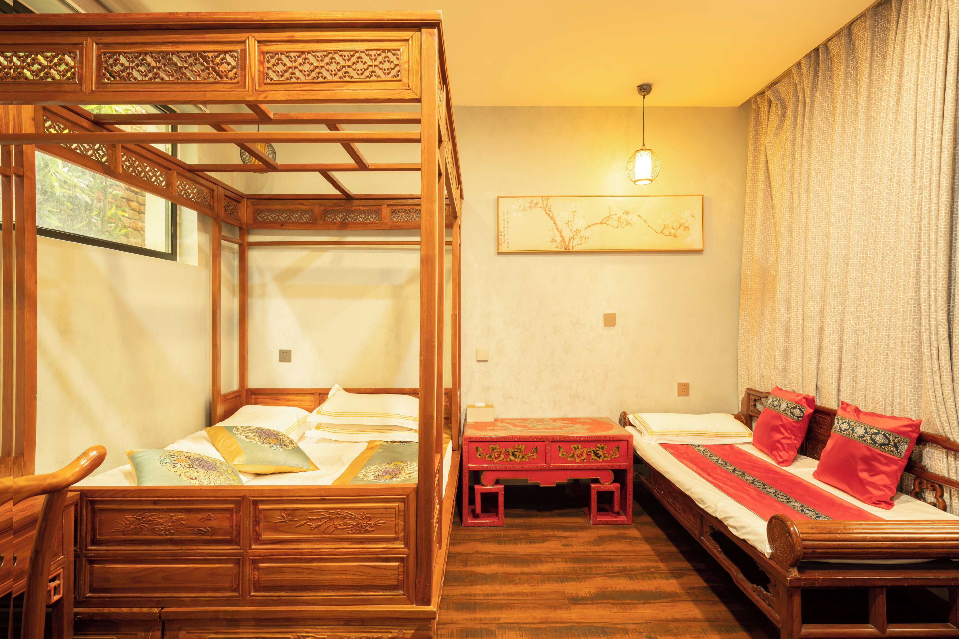 A traditional wooden bed with a canopy, a small wooden table, and a wall-mounted light fixture.
