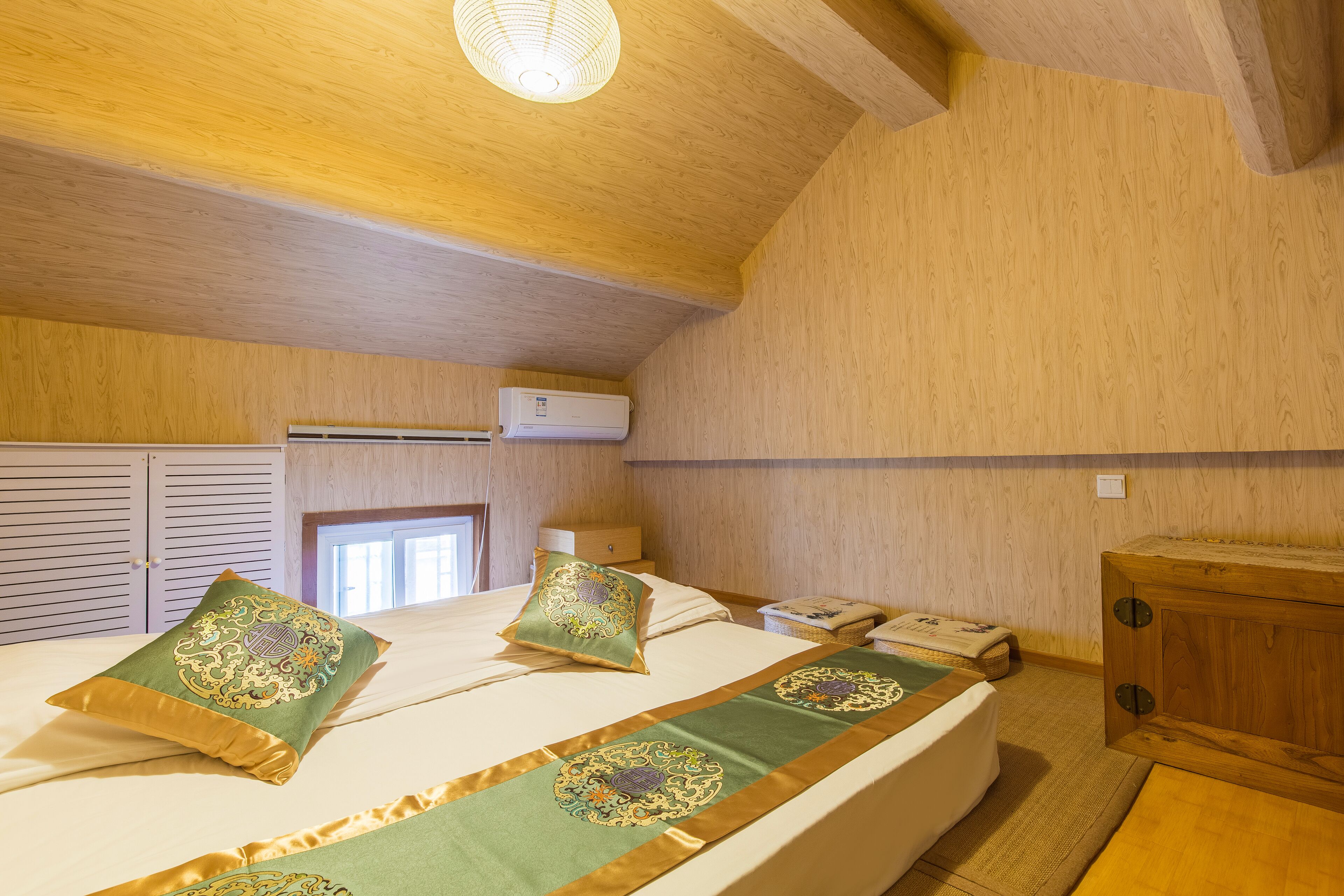 A bedroom with a wooden ceiling, a bed with decorative pillows, a wooden cabinet, and a window.