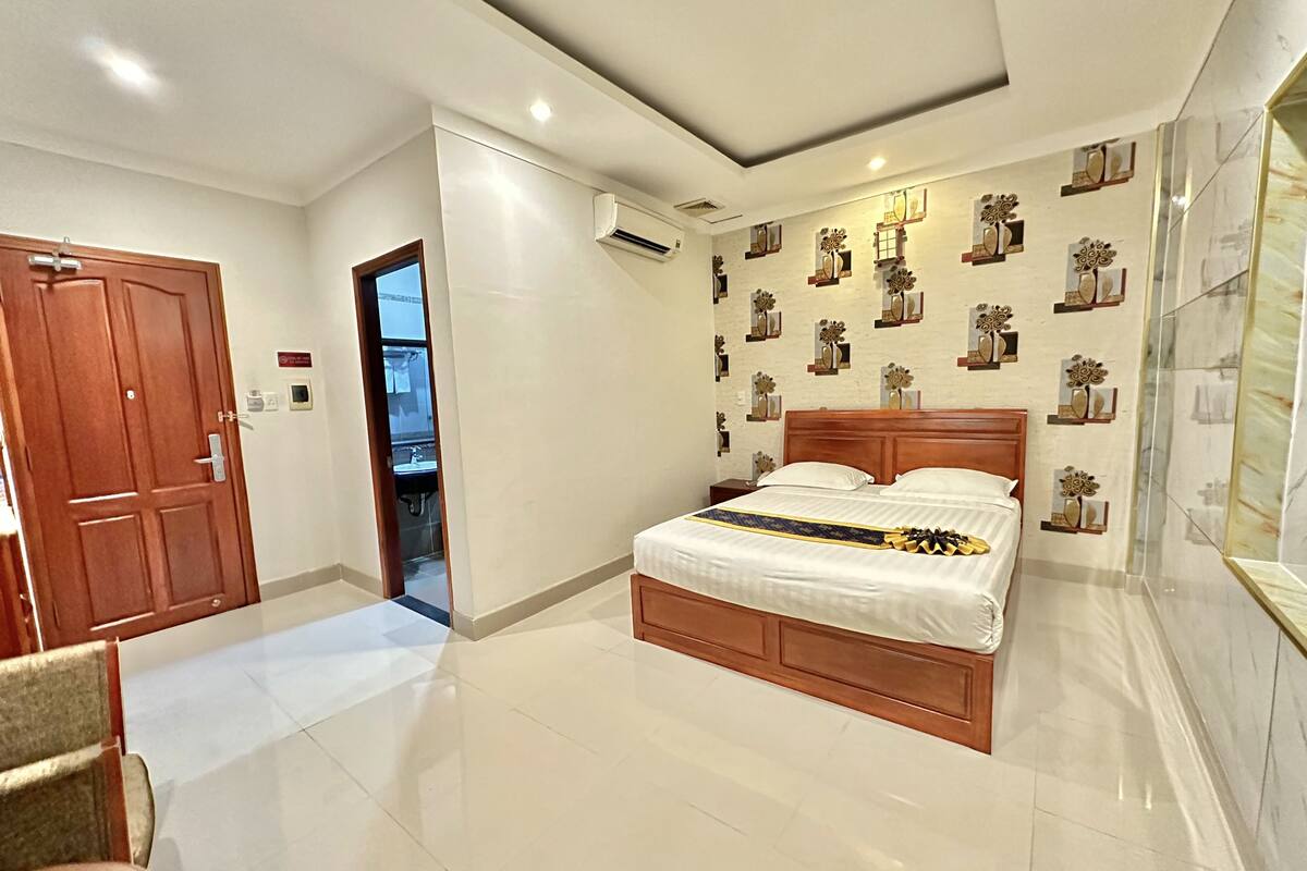 Un dormitorio con cama de madera, paredes blancas y suelo de baldosas.