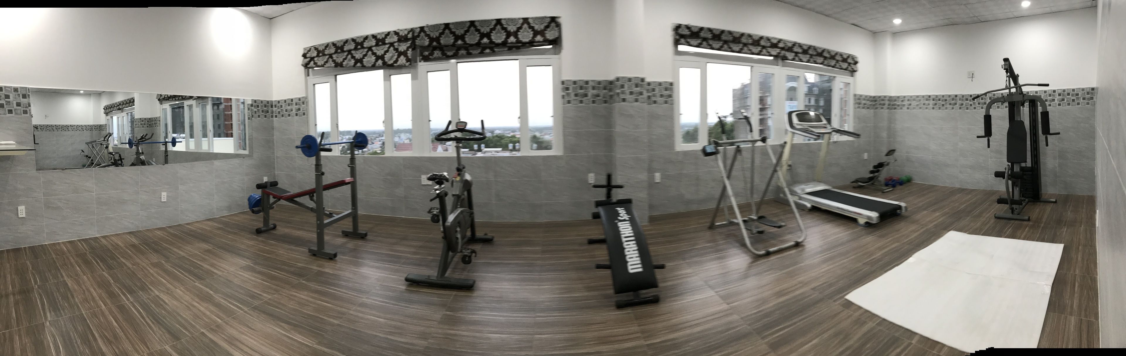 Un gimnasio moderno con diverso equipo de ejercicio, ventanas amplias y un salpicadero de azulejos con diseño.
