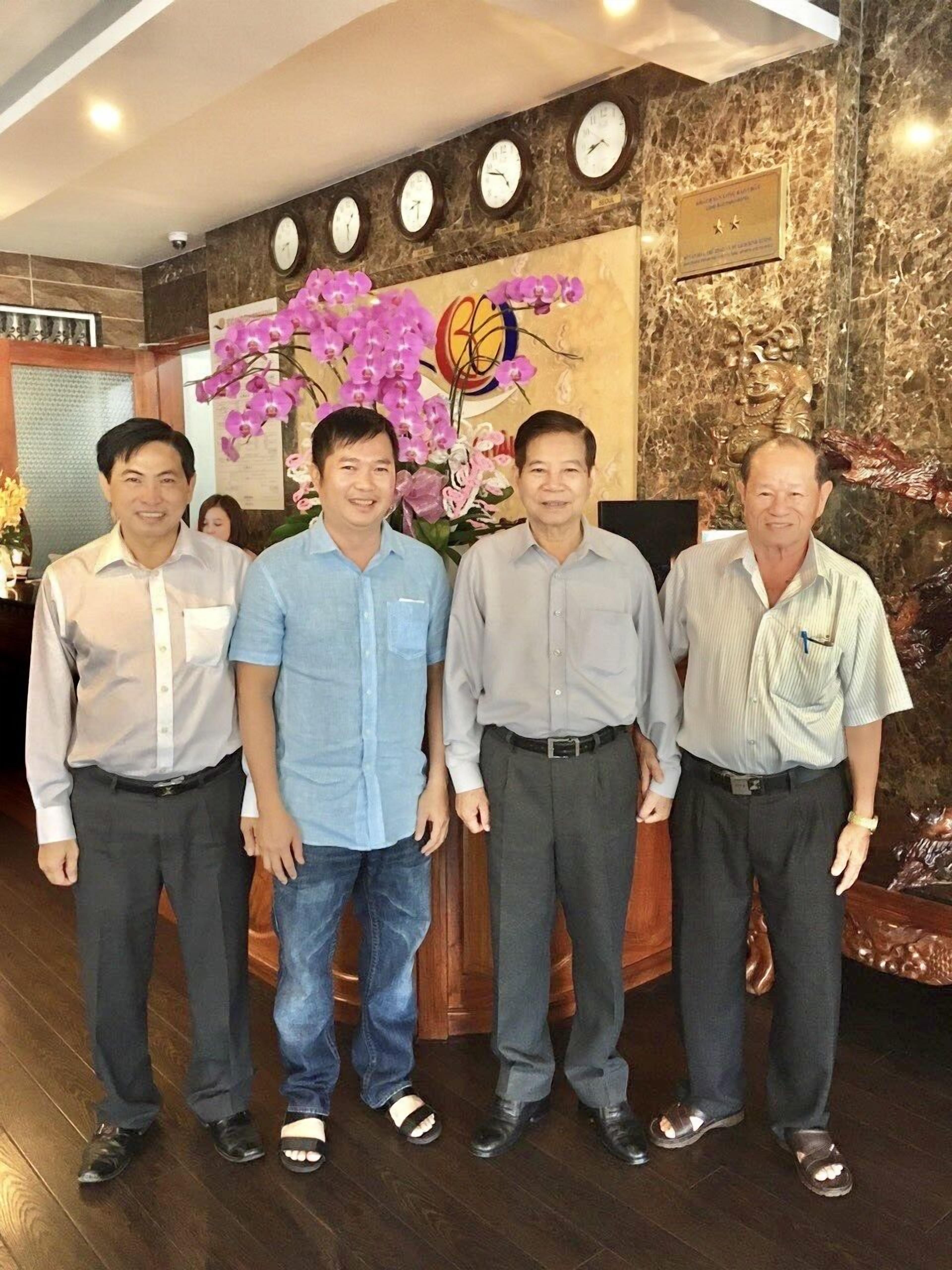 A group of men standing in a lobby with clocks on the wall and a floral arrangement.