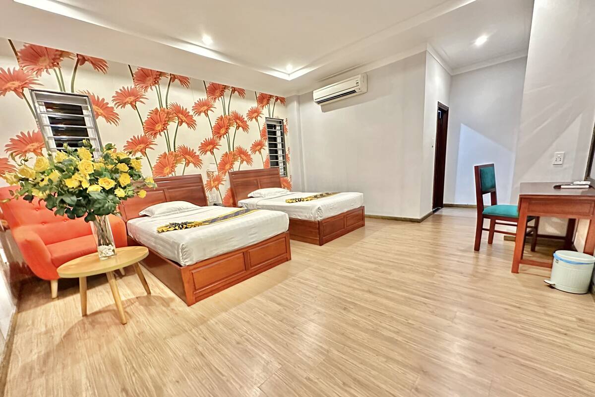 Una habitación de hotel con dos camas de madera, un sofá rojo, una mesita redonda y un escritorio con una silla.