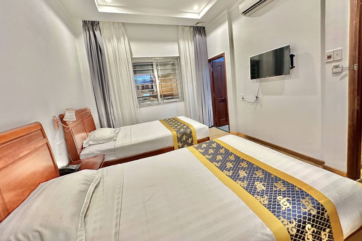Una habitación de hotel con dos camas, un televisor montado en la pared y un equipo de aire acondicionado.