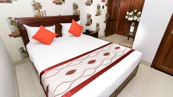 A neatly made bed with a white and red bedspread, two pillows, and a bedside table with a phone and a vase of flowers.