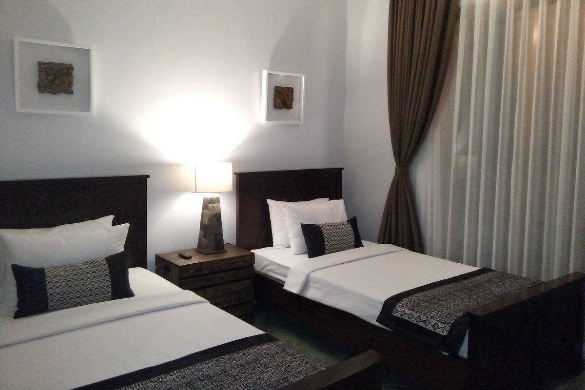 A hotel room with two beds, a nightstand, a lamp, and two framed pictures on the wall.