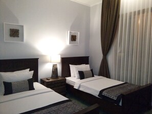 A hotel room with two beds, a nightstand, a lamp, and two framed pictures on the wall. - Casa De Apple (Bandung)