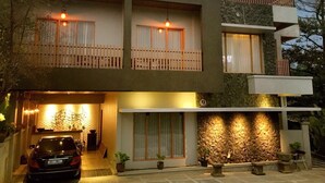 Une maison moderne à deux étages, avec une voiture garée devant, un mur en pierre et un balcon doté d’une balustrade en bois.