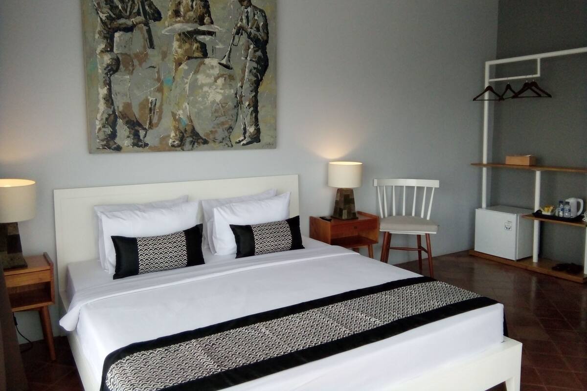 A hotel room with a large bed, two bedside tables, a chair, a small cabinet, and a wall-mounted shelf.
