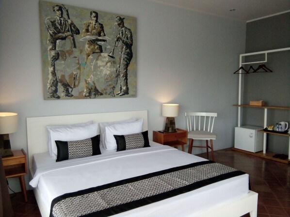 A hotel room with a large bed, two bedside tables, a chair, a small cabinet, and a wall-mounted shelf. - Casa De Apple (Bandung)