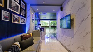 Um hall de hotel moderno com piso de mármore, um sofá com almofadas, quadros nas paredes e uma TV de tela plana.