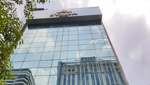 Um edifício moderno alto com janelas de vidro refletivas e um logotipo visível no topo.