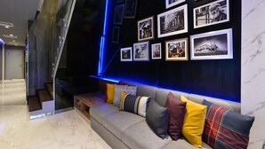 Uma sala de estar moderna com um sofá cinzento, diversos almofadas e uma parede decorada com fotografias emolduradas.