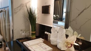 Casa de banho de hotel com parede de mármore, espelho, lavatório e artigos de higiene pessoal.