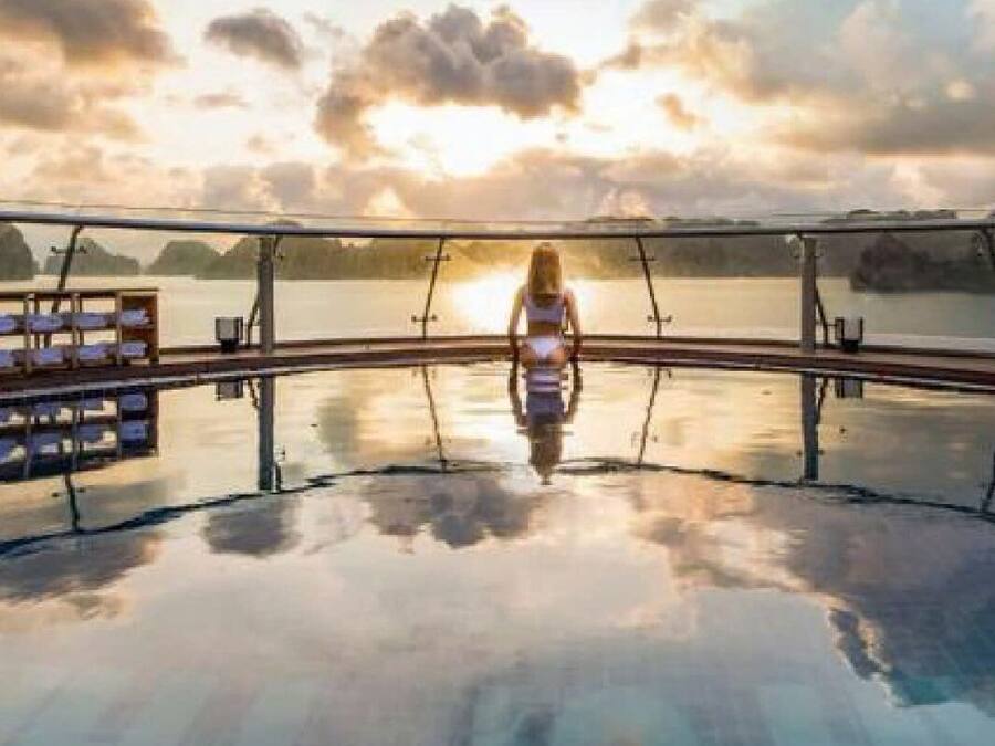 A pool with a glass barrier, a person in the center, and a sunset view.