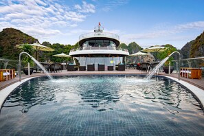 A pool area with a view of a building with a flag on top, surrounded by greenery and hills. - Stellar of the Seas (Hanoi)