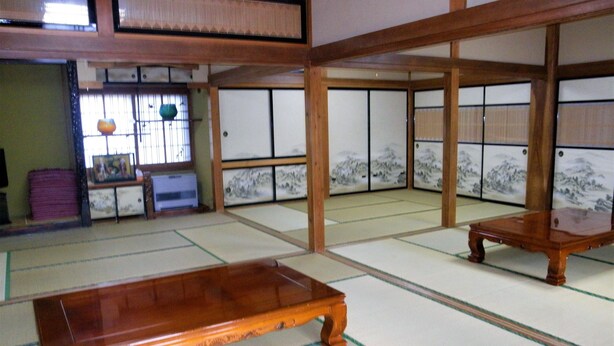 Ein Raum mit Tatami-Matten, einem Holztisch und einer Wand mit einer Kunstausstattung, versehen mit Schiebetüren.