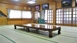 Ein Raum mit Tatami-Matten, einem niedrigen Tisch, Holzwänden und verschiebbaren Türen mit Blick ins Freie.